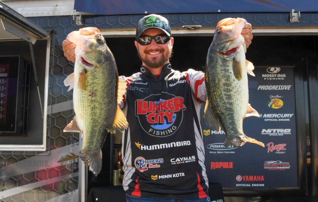 Angler Alex Wetherell holds up two largemouth bass on the weigh-in stage